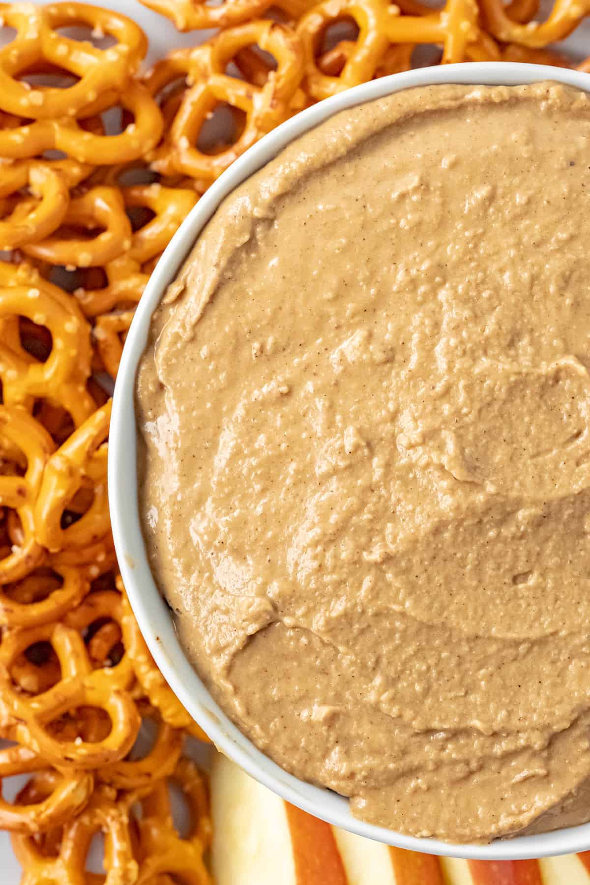 closeup image of the hummus in a white bowl with pretzels to the left side