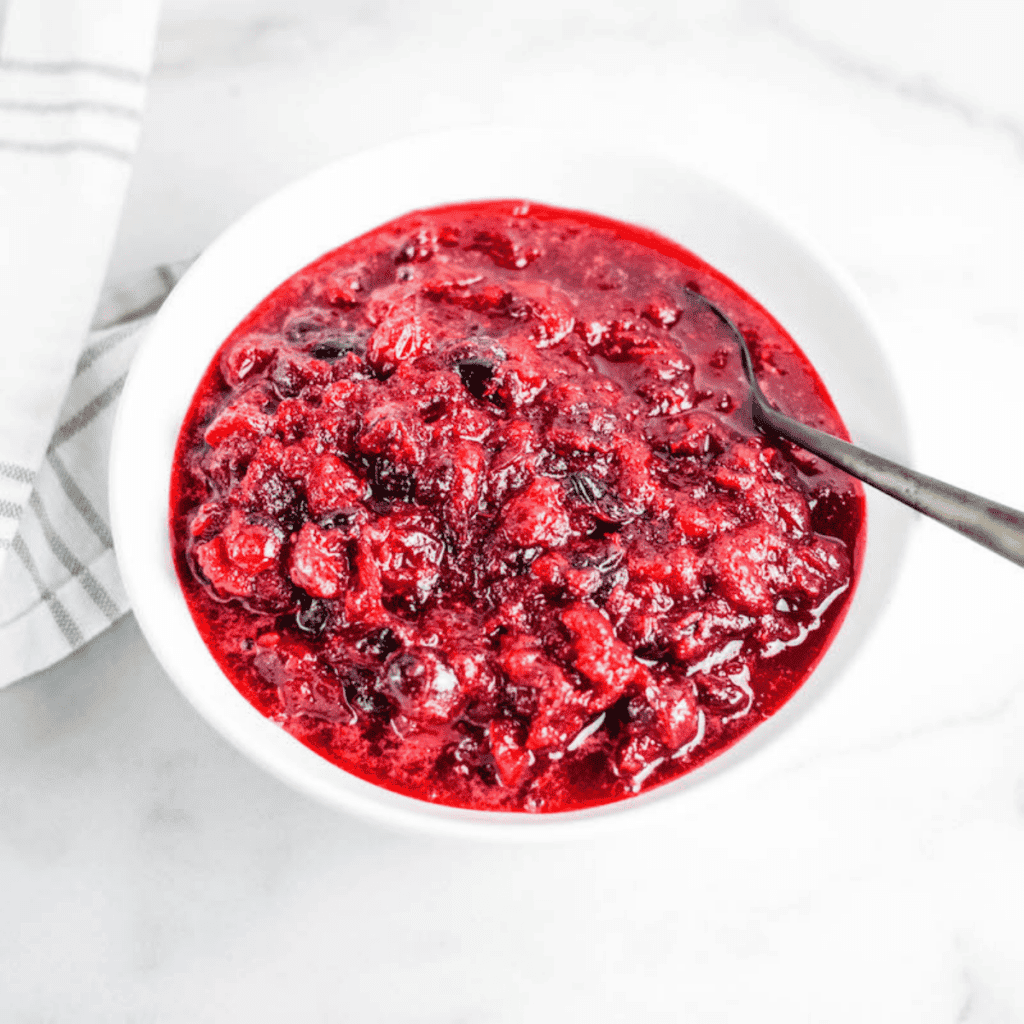 white bowl of healthy cranberry sauce with a white and grey striped tea towel at the side