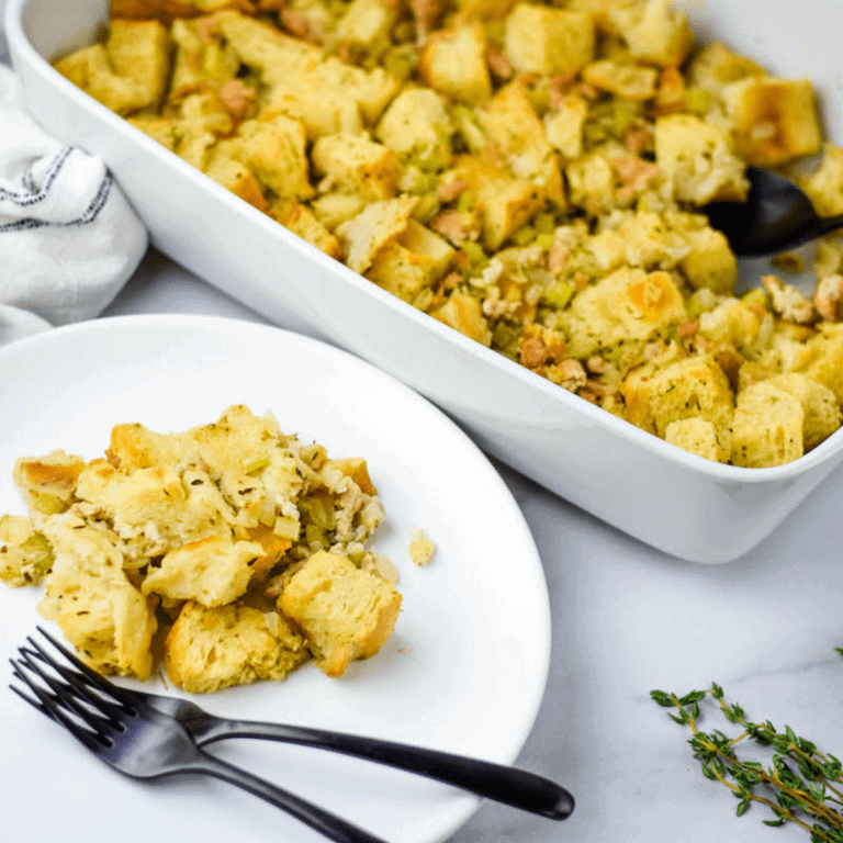 sourdough stuffing on two white plates with black forks and the casserole dish in the background