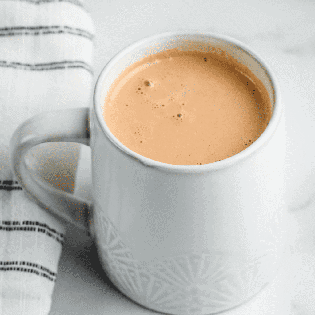 creamy & healthy hot chocolate in a white mug with a black and white striped tea towel beside it