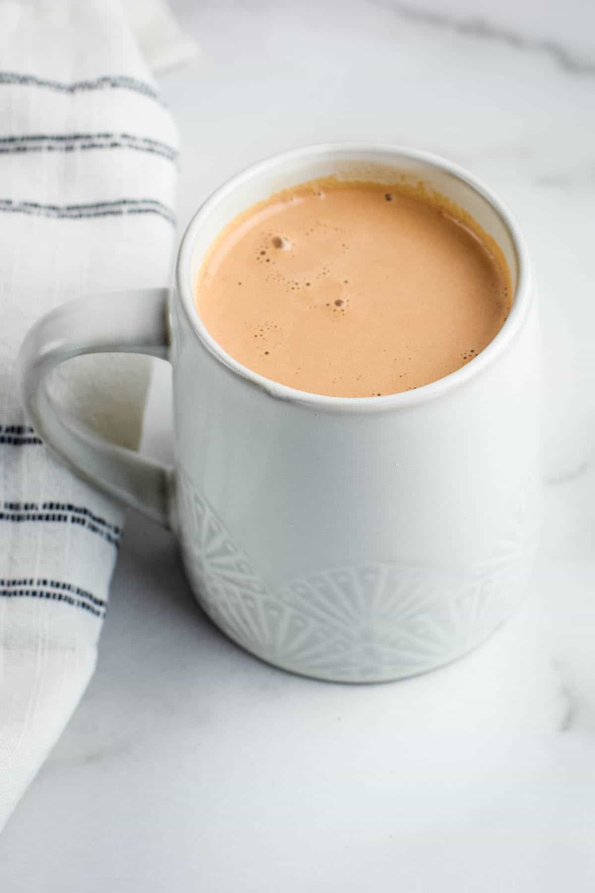 finished healthy hot chocolate in a white mug with a black and white striped tea towel beside it