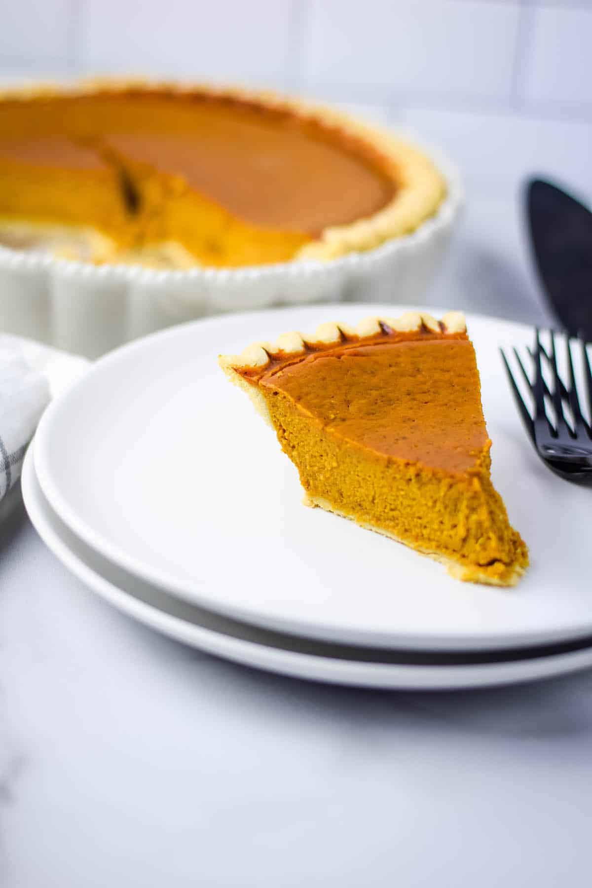 slice of homemade pumpkin pie on a white plate with black fork beside it