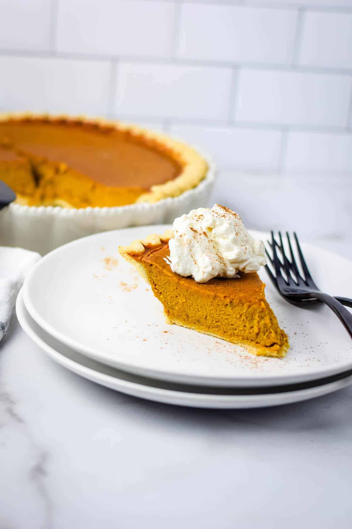 fresh slice of healthy pumpkin pie on white plate with fresh homemade whipped cream