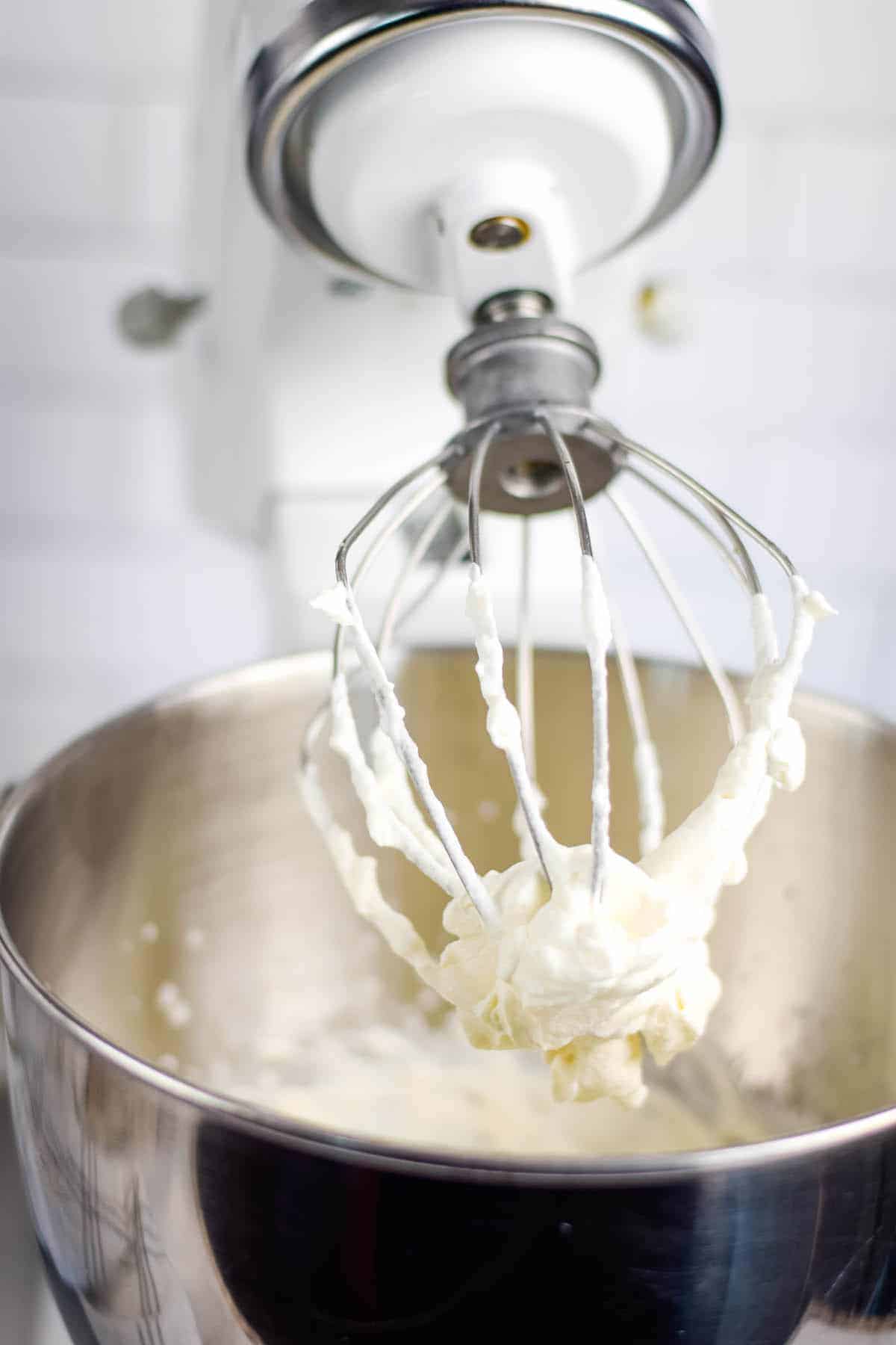 stand mixer with the whisk attachment and homemade maple whipped cream on the whisk