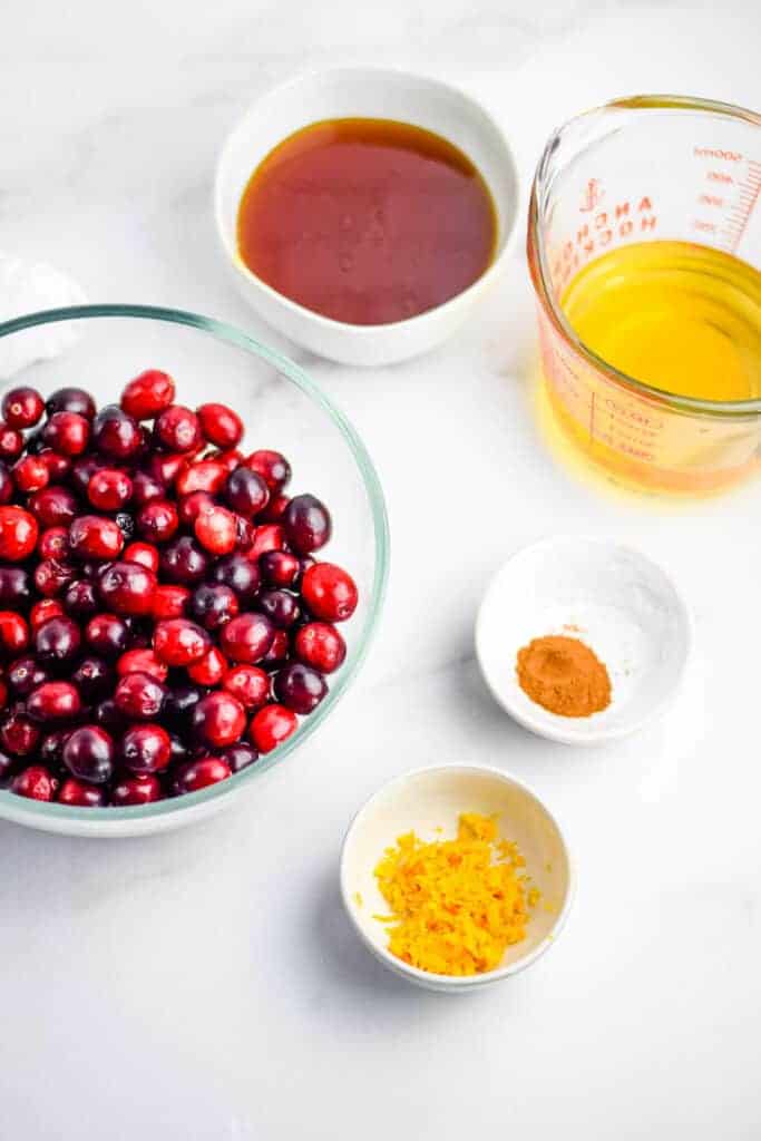 ingredients shot of fresh cranberries, orange zest, cinnamon, apple juice, and raw honey in bowls