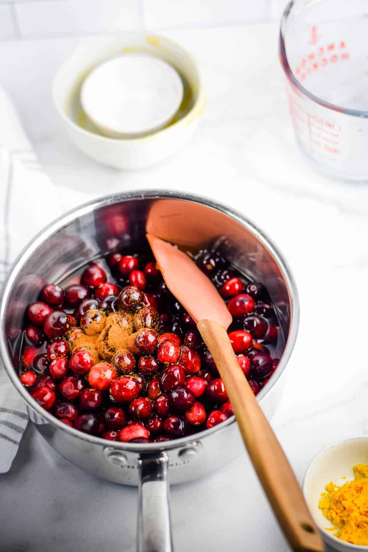 adding the cranberries, honey, apple juice, and cinnamon to the sauce pan with a spatula stirring the ingredients