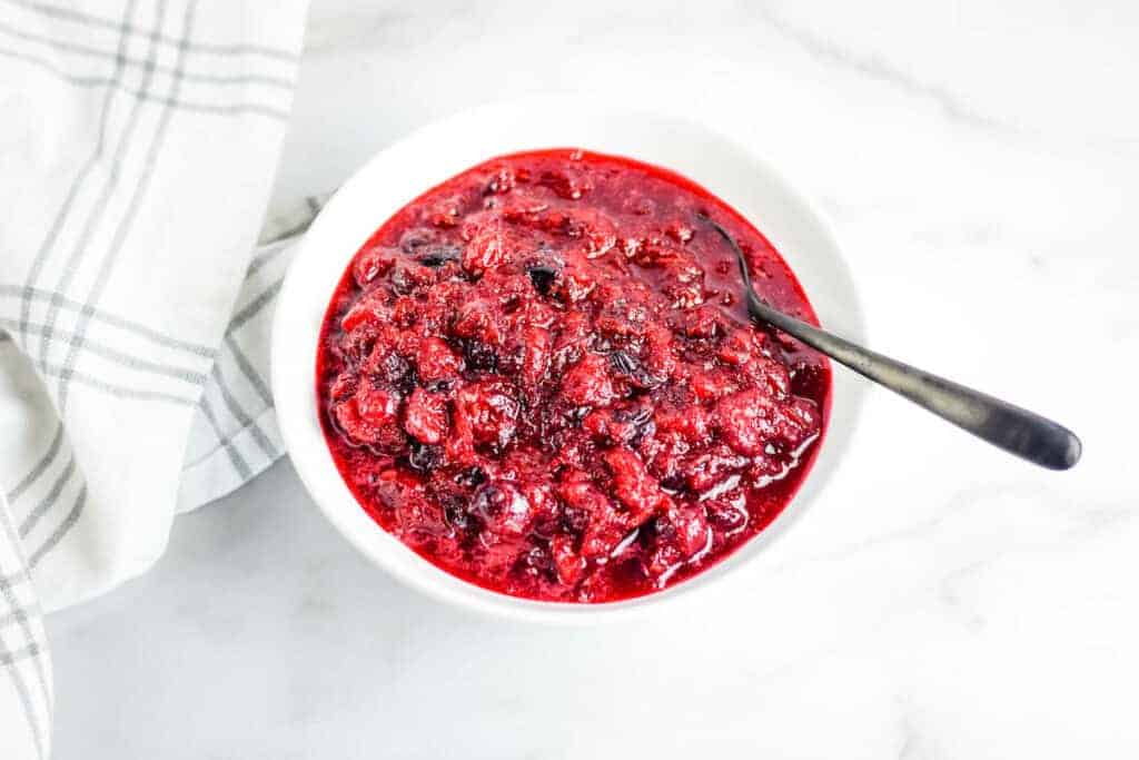 white bowl with finished honey sweetened cranberry sauce with a black spoon at the side