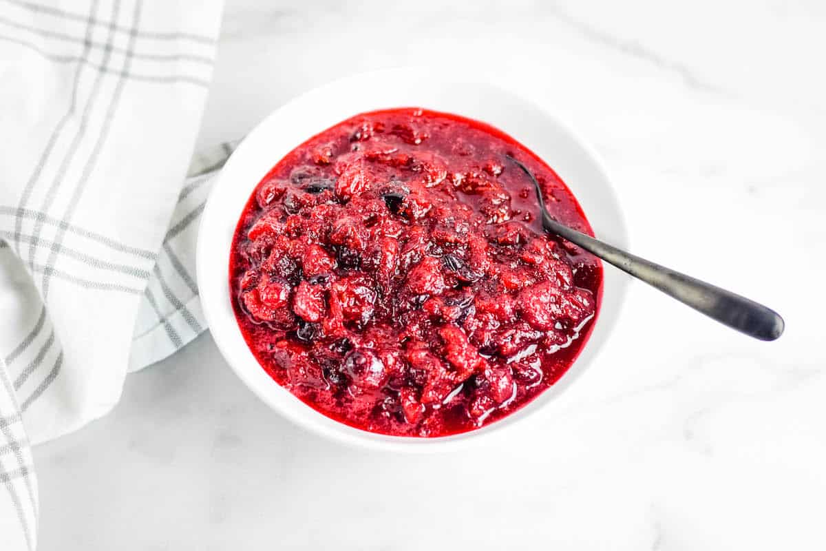 white bowl with finished honey sweetened cranberry sauce with a black spoon at the side