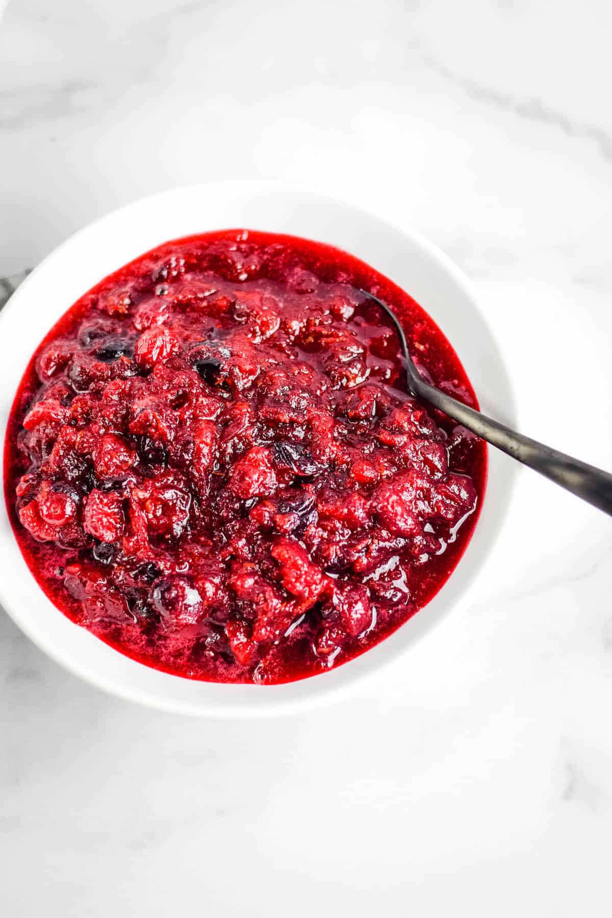 white serving bowl of healthy honey sweetened cranberry sauce with a black spoon