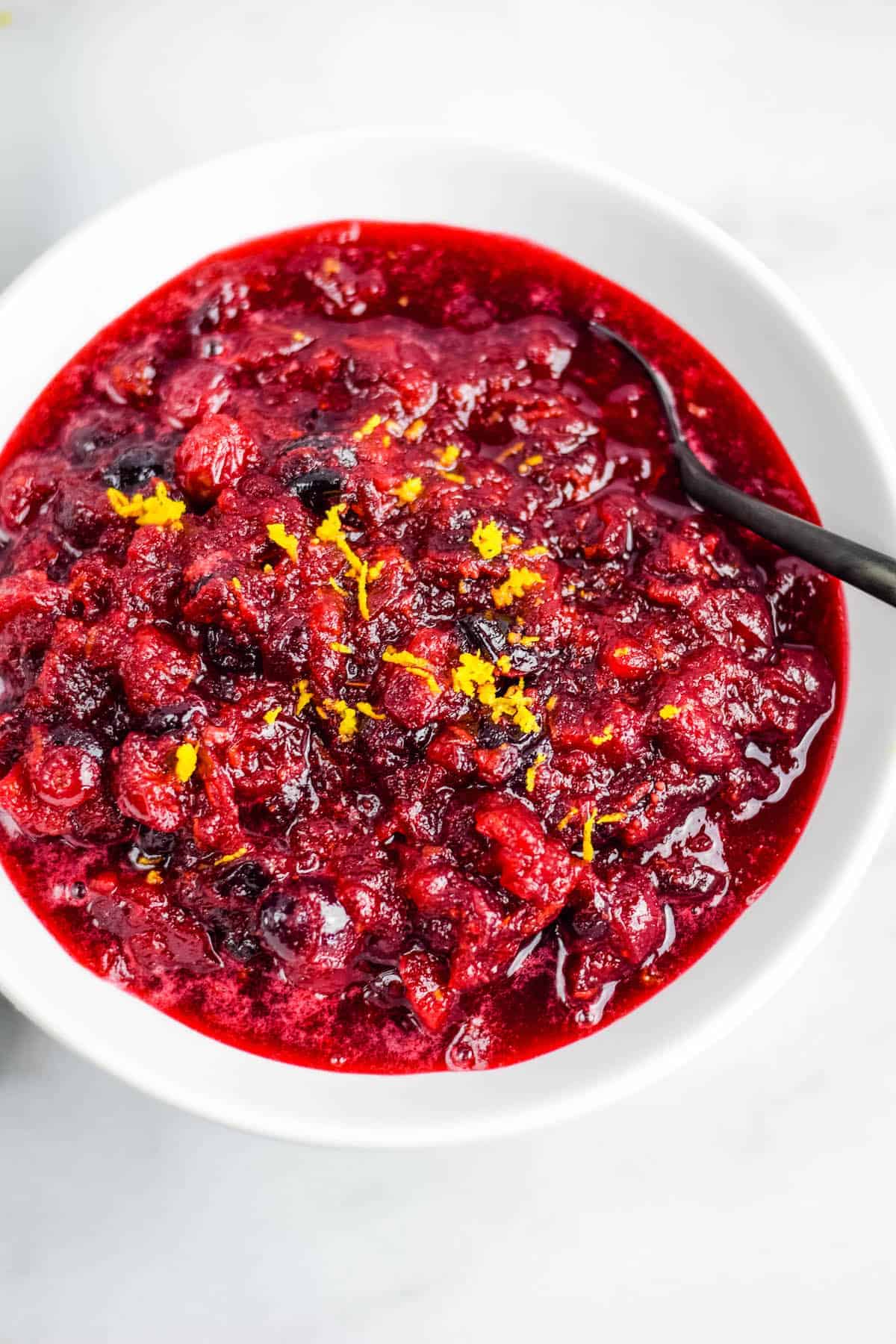 close up image of naturally sweetened cranberries in a white bowl with orange zest on top