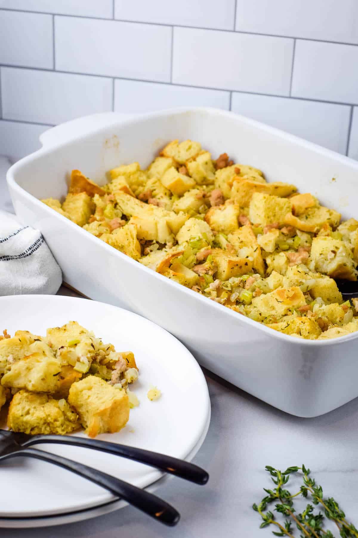 finished sourdough stuffing in a white casserole dish with two white plates and black forks