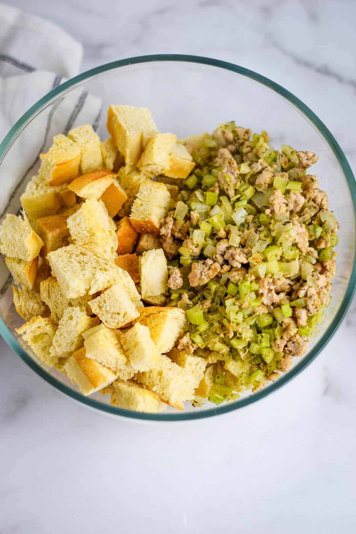 large glass bowl with the toasted sourdough bread cubes and celery, onion, and sausage mixture