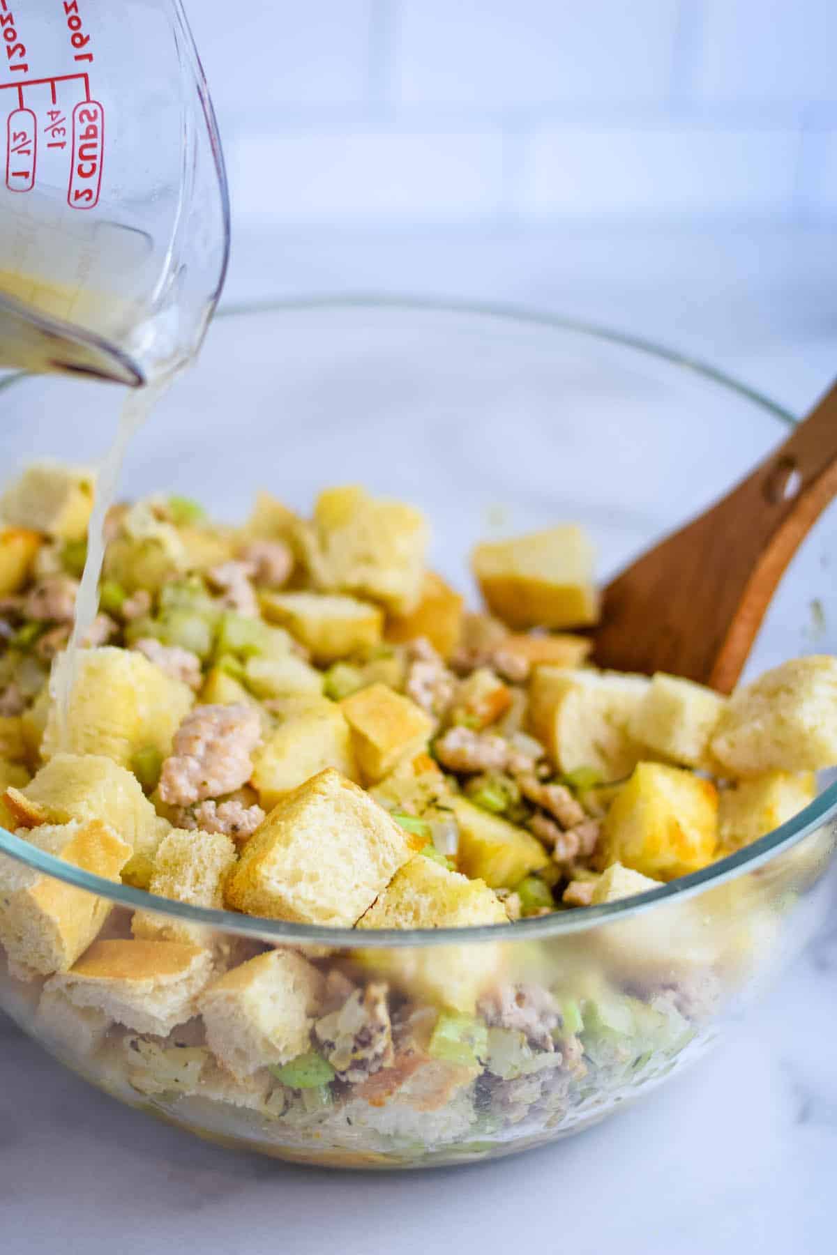 pouring the chicken broth over the stuffing mixture in a large glass pan 