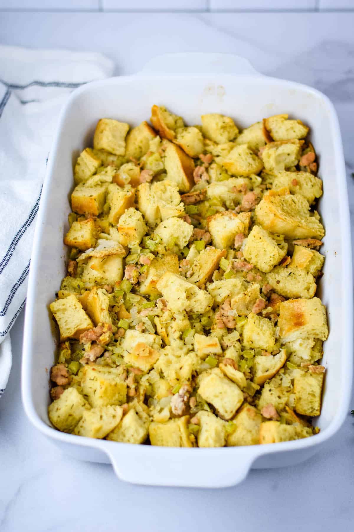 white casserole dish with the sourdough stuffing with sausage and black and white tea towel resting on the side