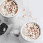 two coffee mugs with healthy peppermint mocha topped with homemade whipped cream and crushed candy cane pieces.