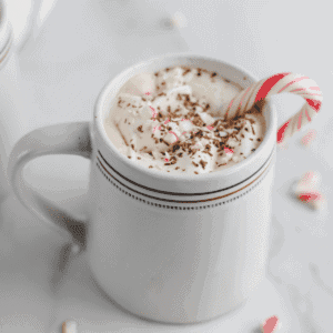 white mug with peppermint mocha and whipped cream on top with a mint candy cane resting inside
