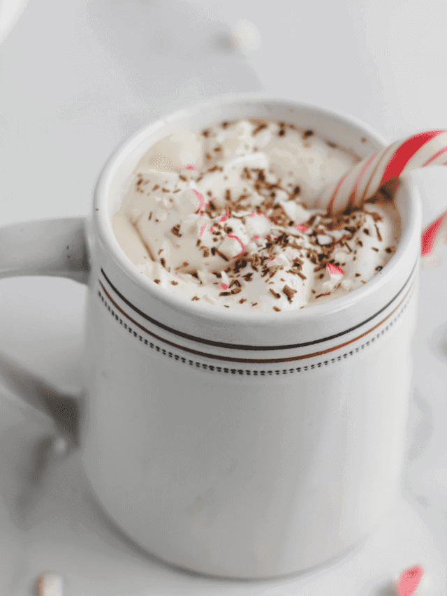 white mug with peppermint mocha and whipped cream on top with a mint candy cane resting inside
