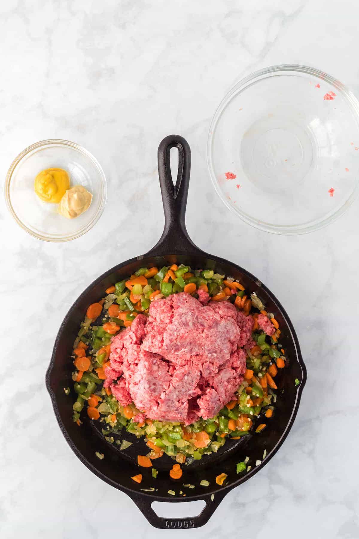 adding the ground beef to the sautéed vegetables inside of the cast iron skillet