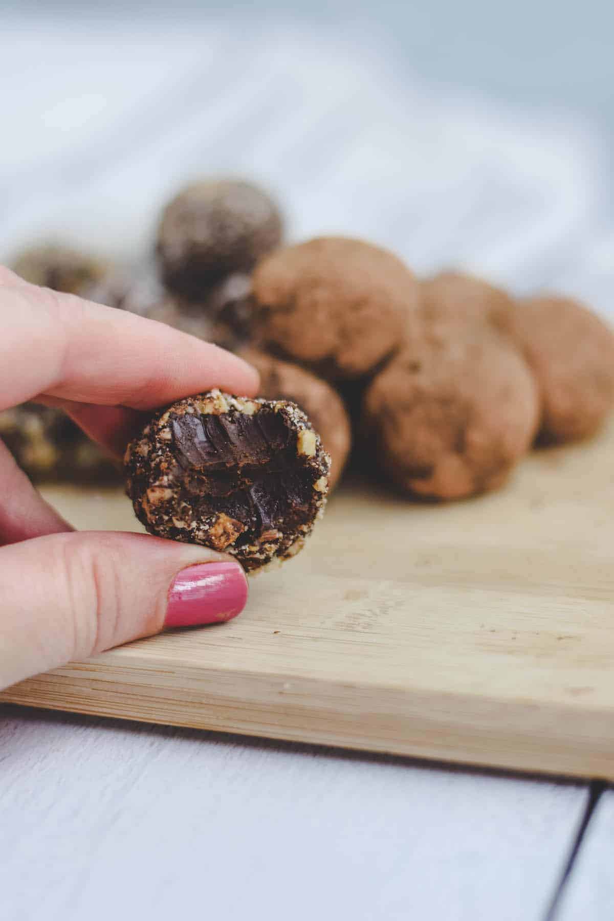 bite shot of a chocolate truffle with rolled truffles in the background on a wooden board