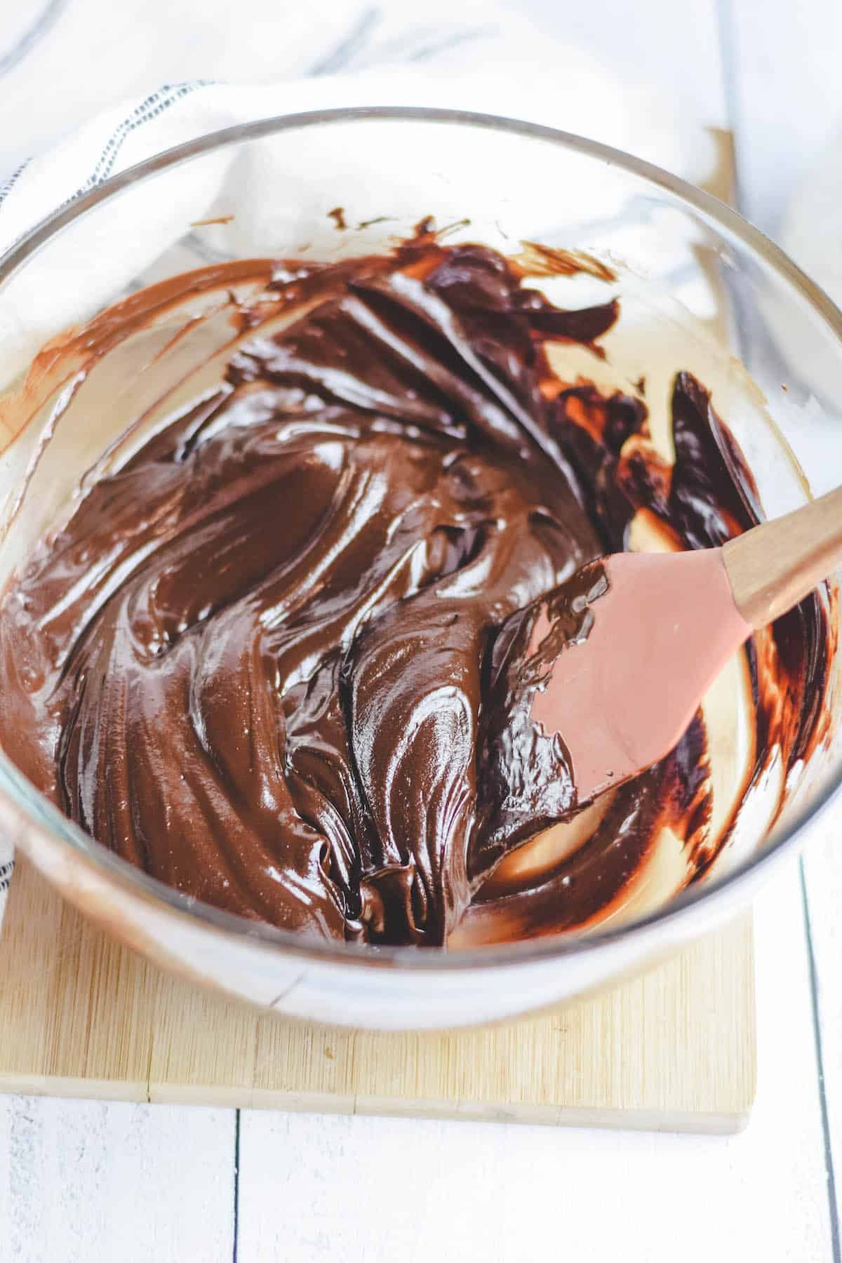 a glass bowl of chocolate ganache with a spatula