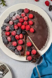 chocolate raspberry tart on a white platter with silver serving utensil.