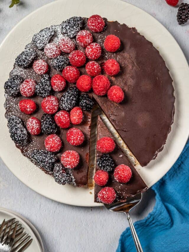 chocolate raspberry tart on a white platter with silver serving utensil.