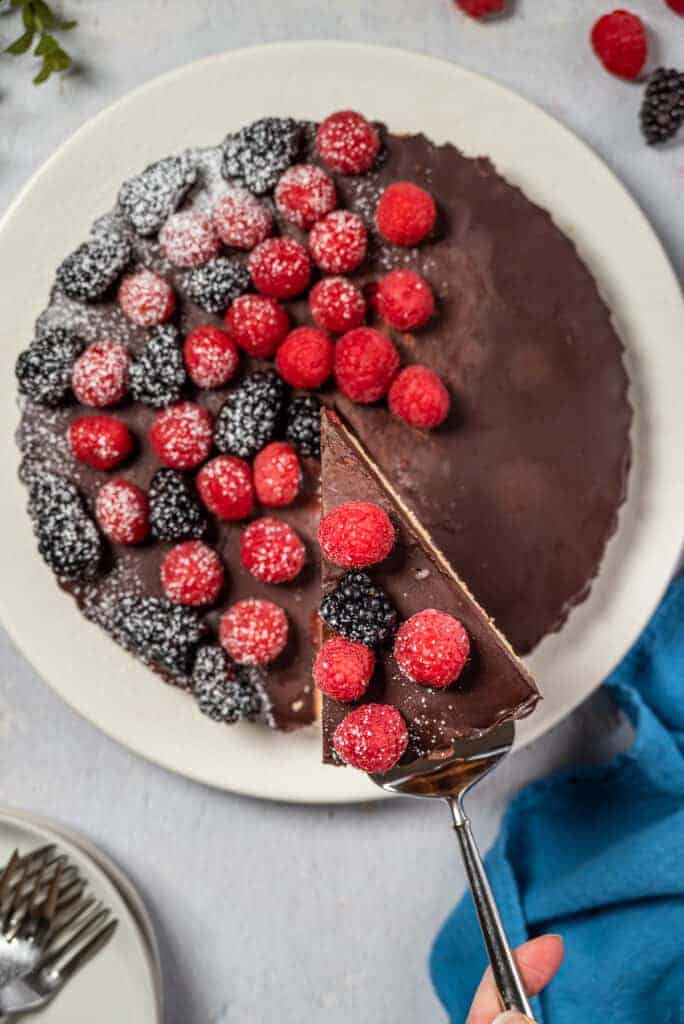 white plate with the healthy chocolate raspberry tart and serving utensil with blue linens