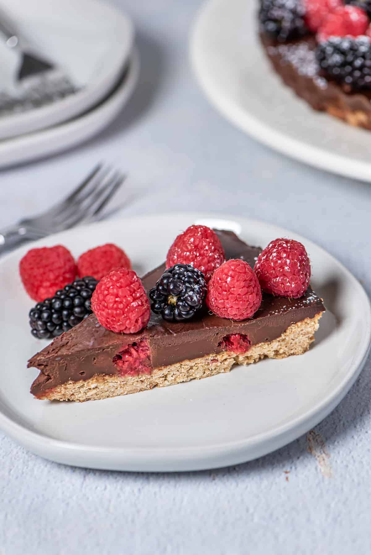 white plate with a slice of chocolate raspberry tart with fresh berries