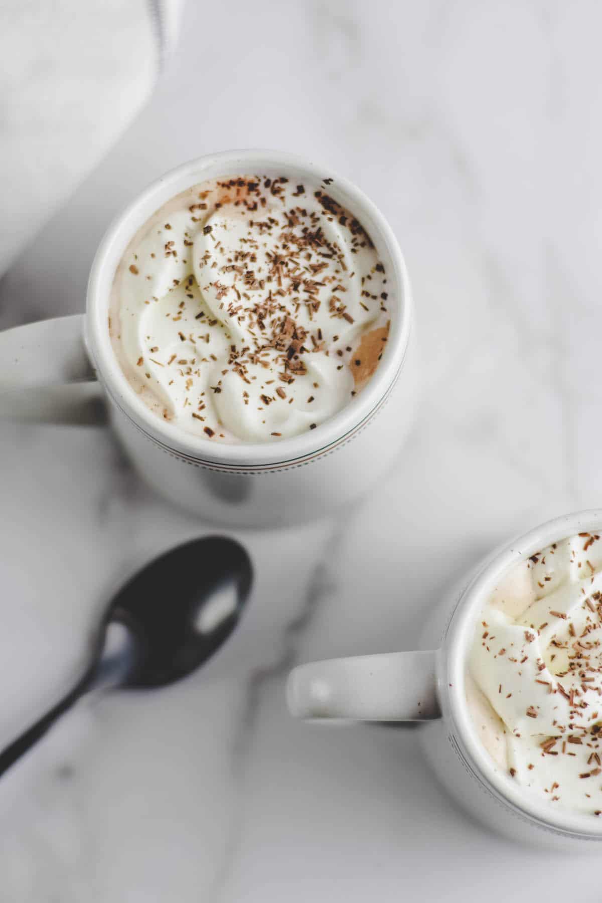 two white mugs of peppermint mocha with whipped cream and chocolate shavings on top 