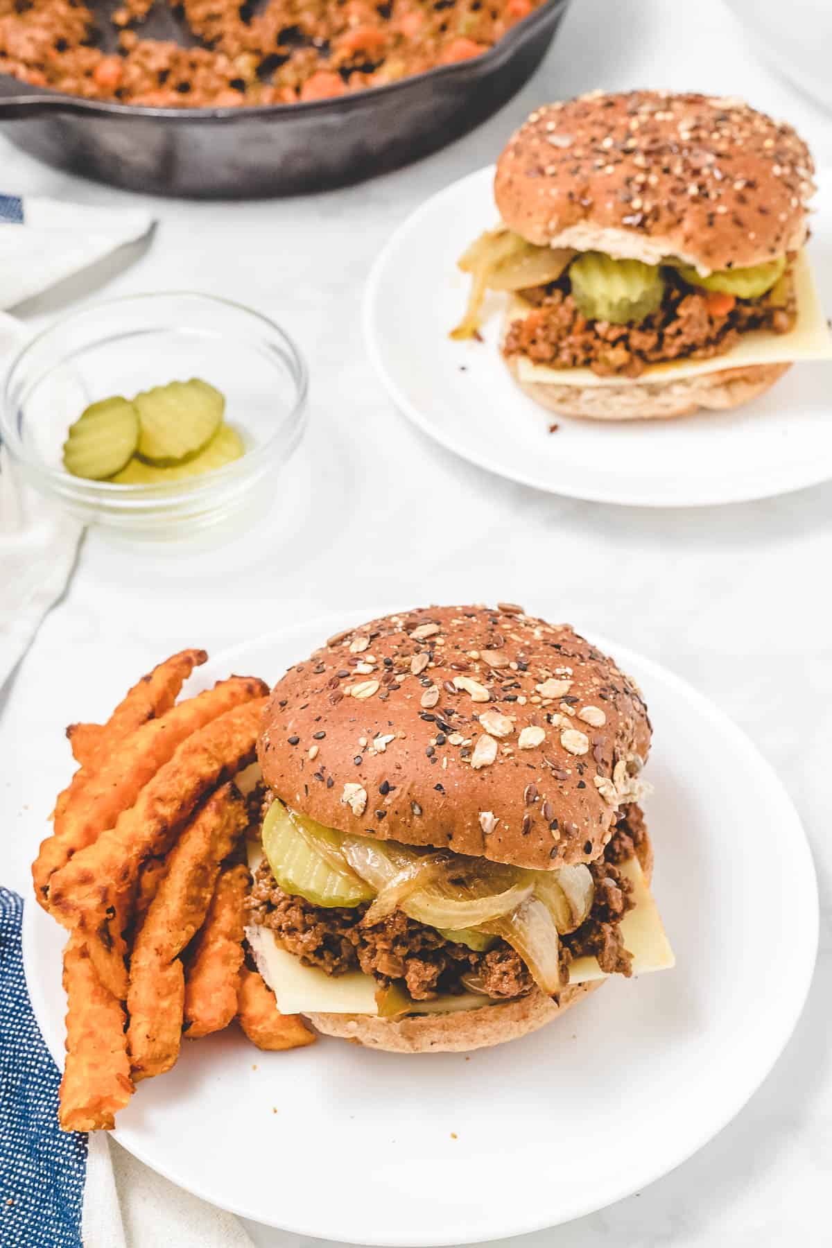 sloppy joes on whole wheat buns with sweet potato fries beside them on a white plate