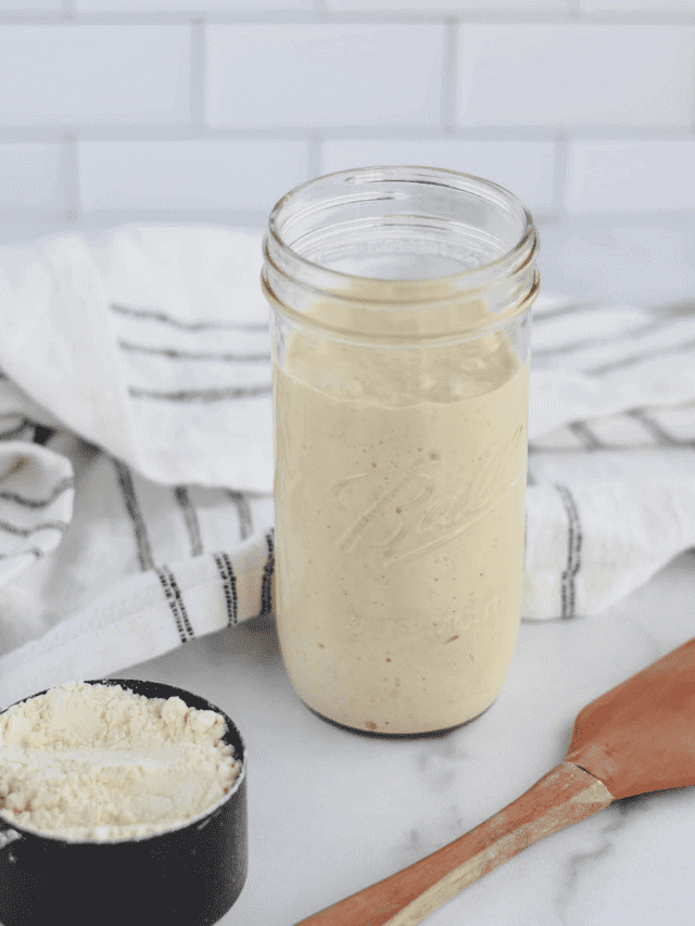 einkorn sourdough starter in a mason jar with a spatula and black measuring cup