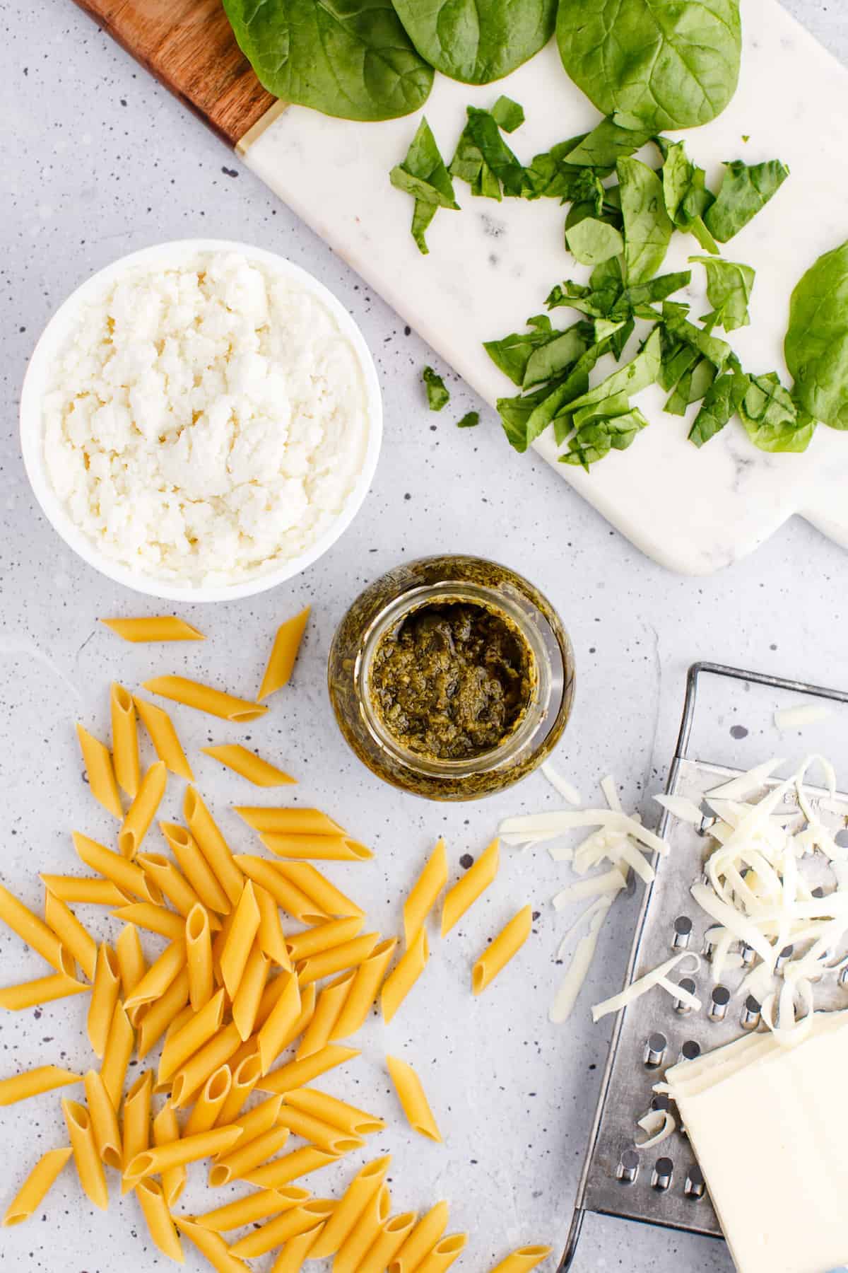 ingredients for the pesto pasta in small bowls and herbs on the cutting board