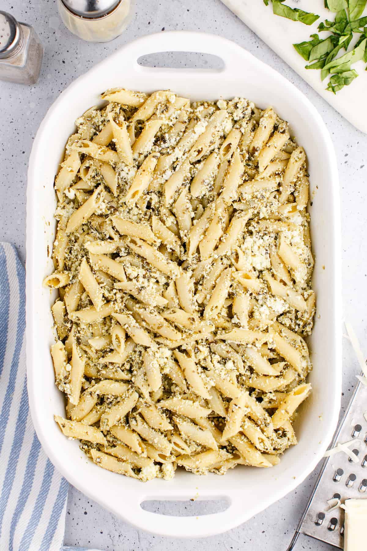 adding the pasta, ricotta, and pesto mixture to a large white casserole dish 