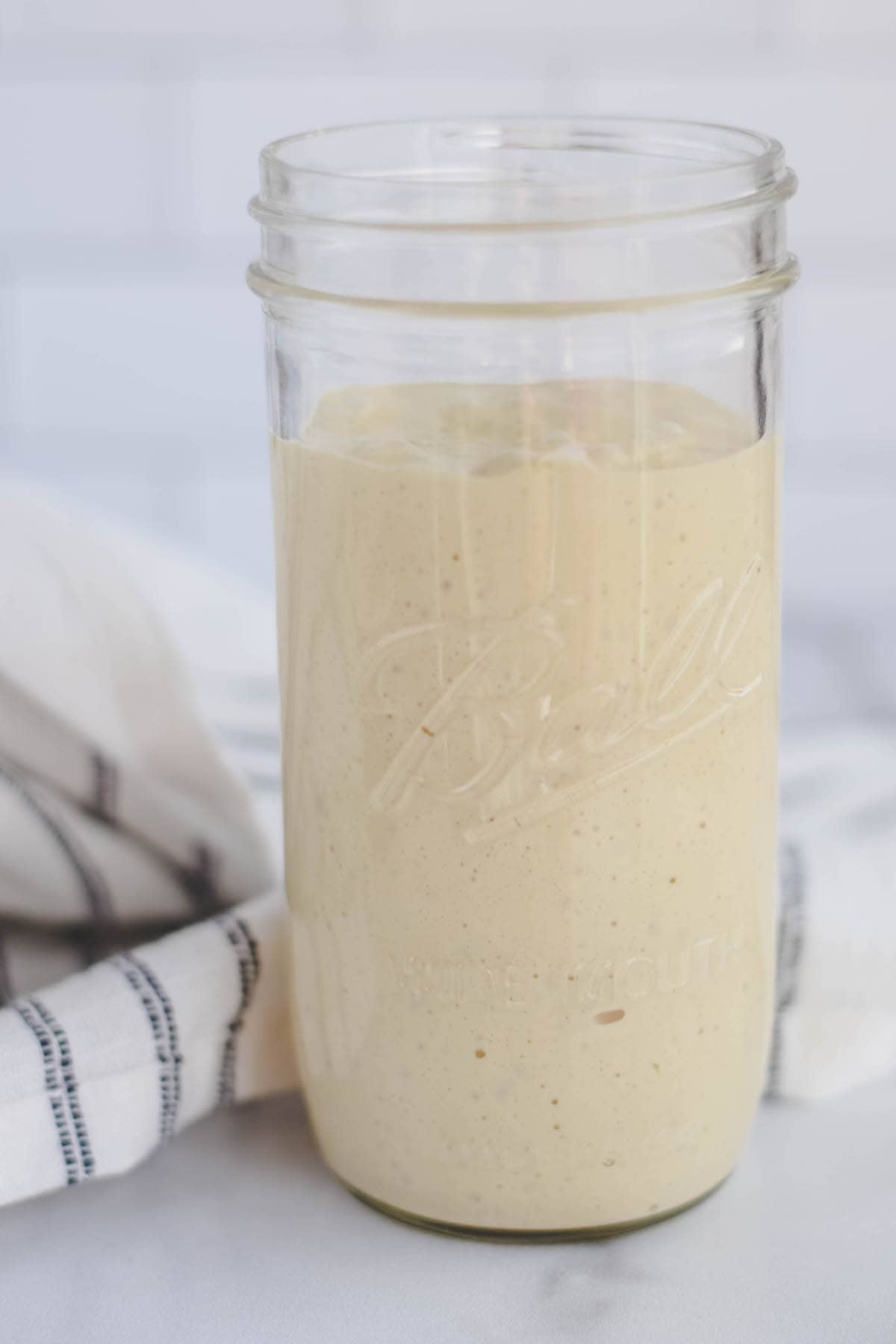 large mason jar filled with einkorn sourdough starter and a black and white striped tea towel to the side