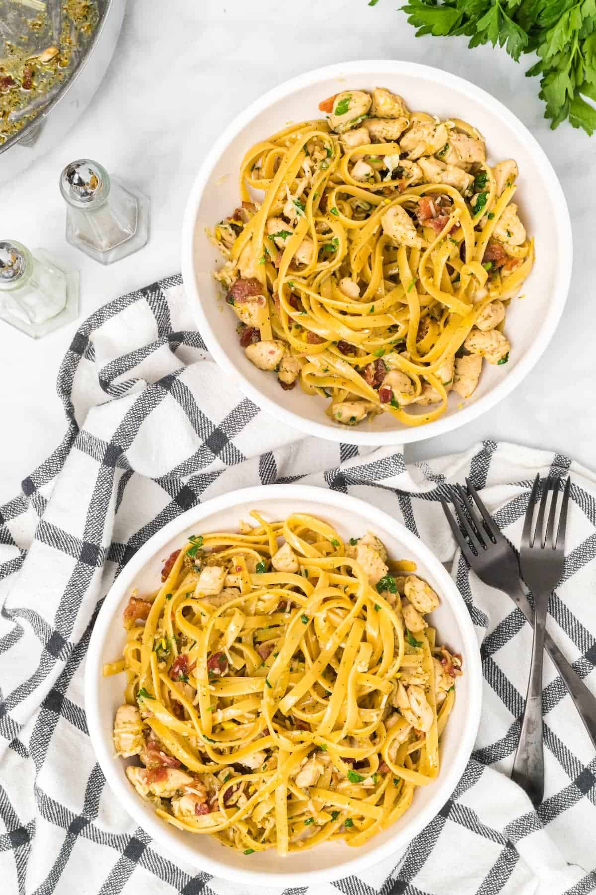 two white pasta bowls filled with chicken bacon carbonara with two black forks to the side.