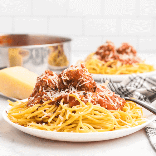 white plate of spaghetti with meatballs marinara on top