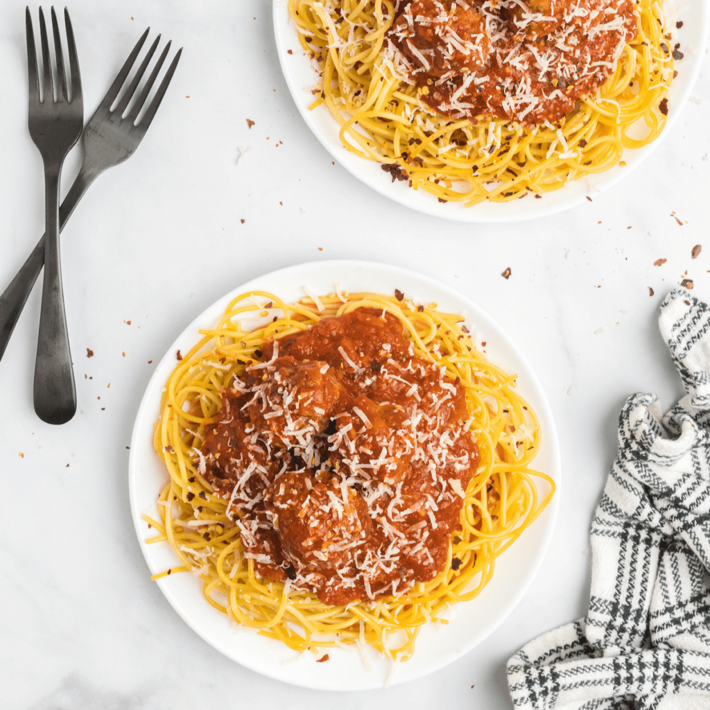 two white plates of spaghetti noodles with meatballs and marinara sauce