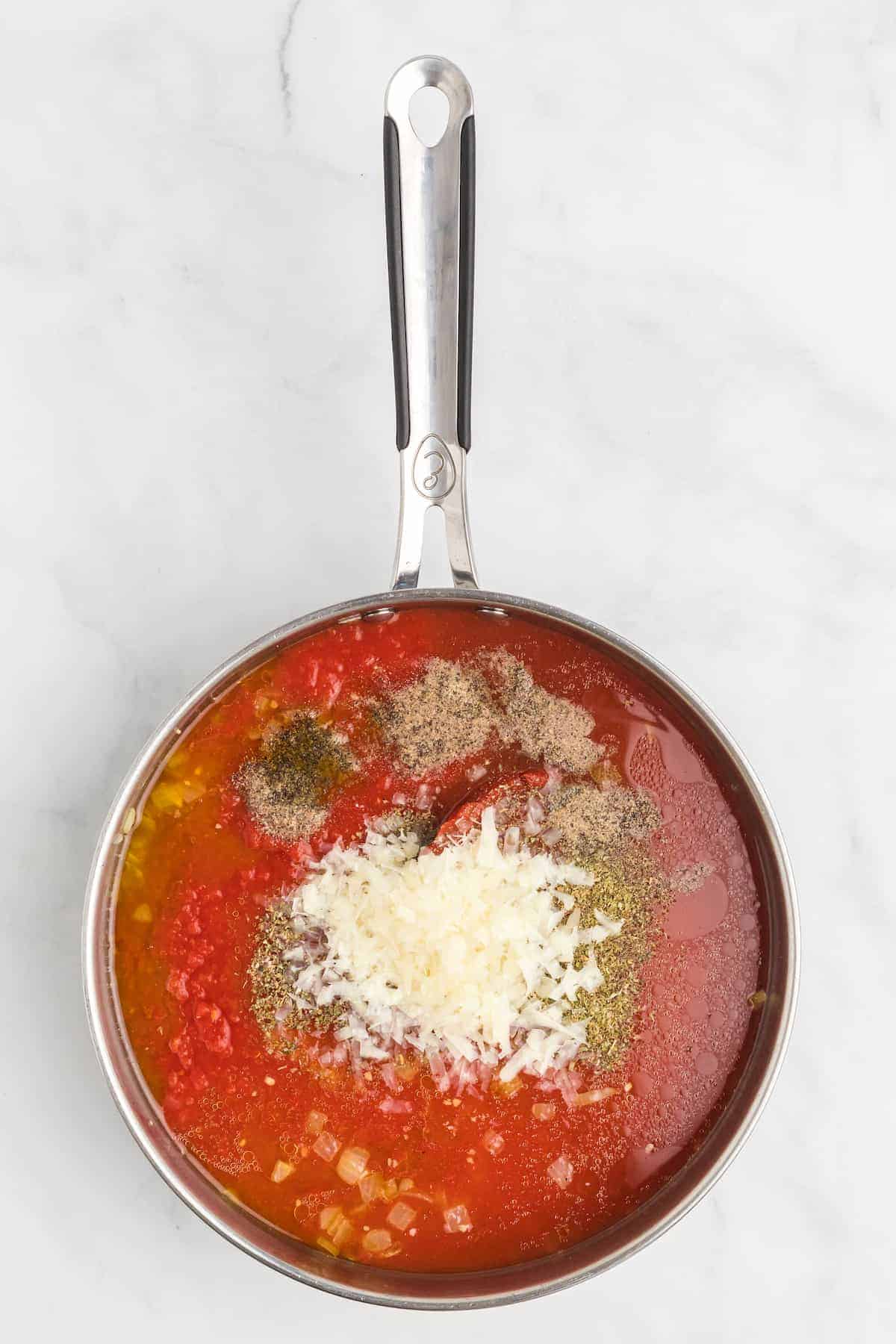 seasonings and parmesan cheese on top of the tomatoes in the saucepan