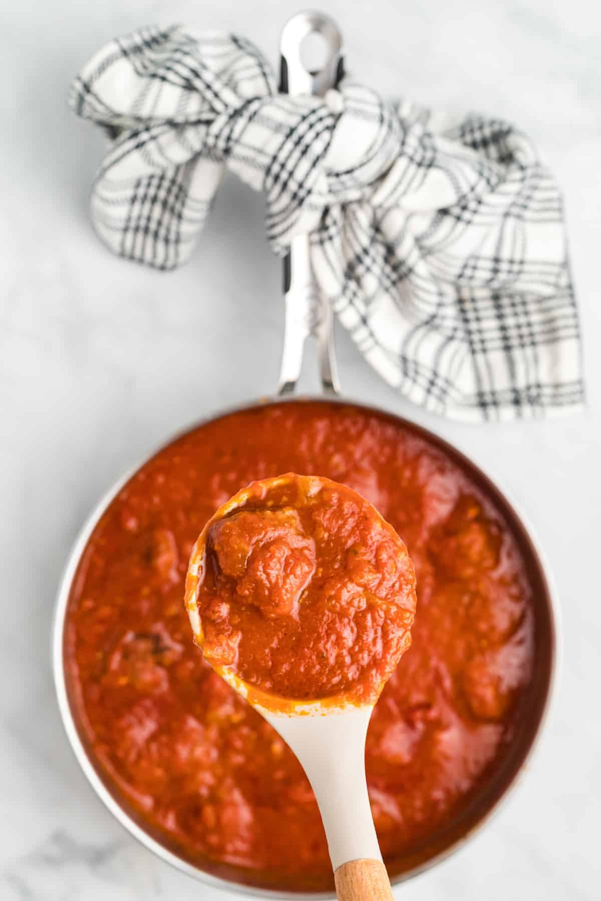 meatballs and marinara sauce on a serving spoon with the pot below it.