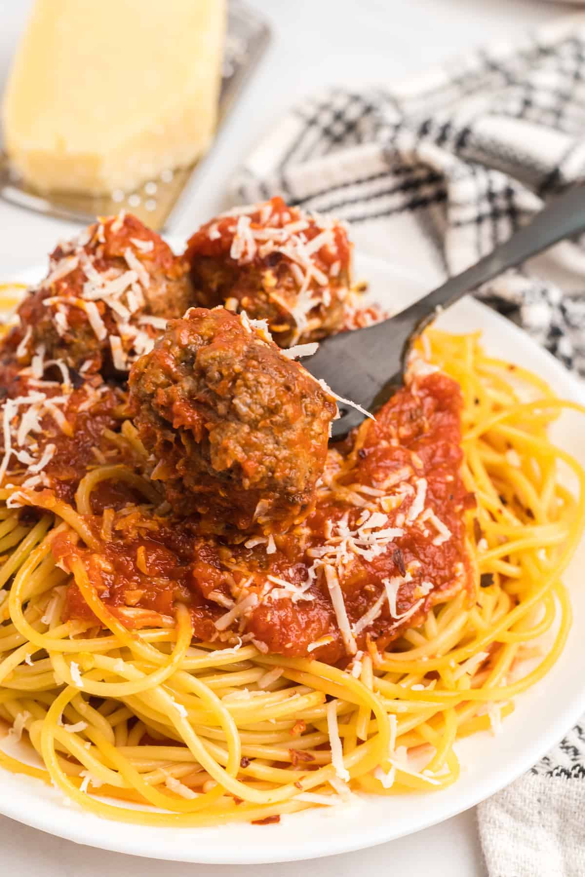 white plate of meatball marinara with a black fork holding a meatball.