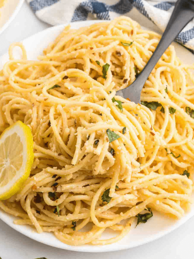 creamy lemon pasta on a white plate with a black fork sticking out of it on the side.