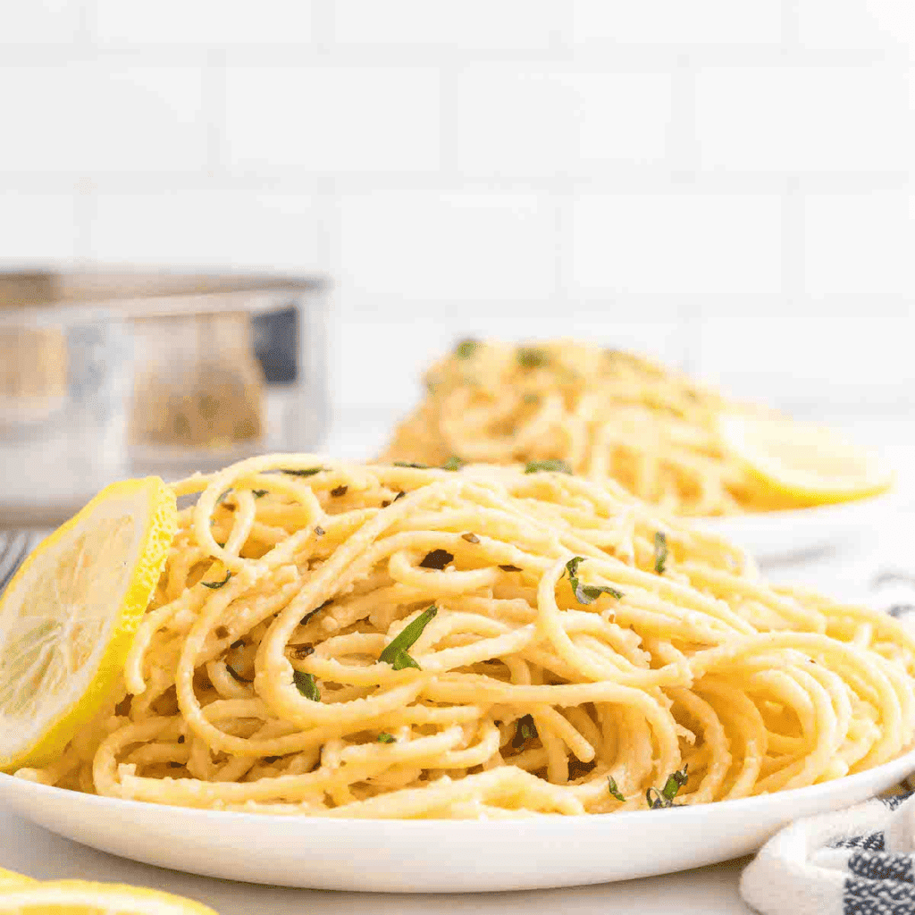 white plate of creamy lemon pasta with a lemon slice to the side.