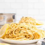 white plate of creamy lemon pasta with a lemon slice to the side.