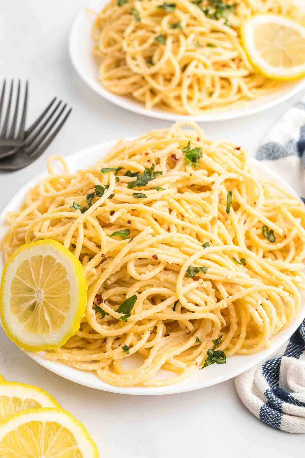 two white plates of creamy lemon pasta with black forks to the side