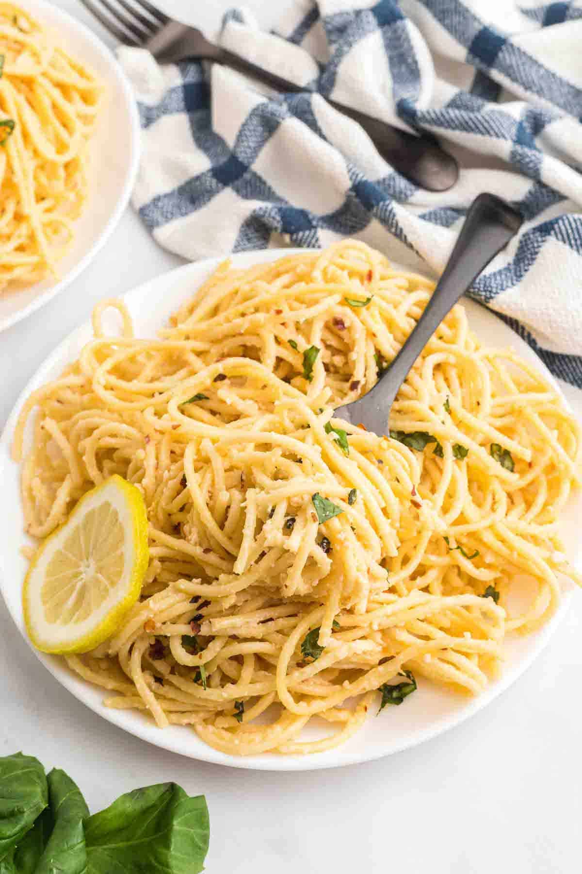 white plate of creamy lemon pasta with a black fork and blue & white tea towel in the back.