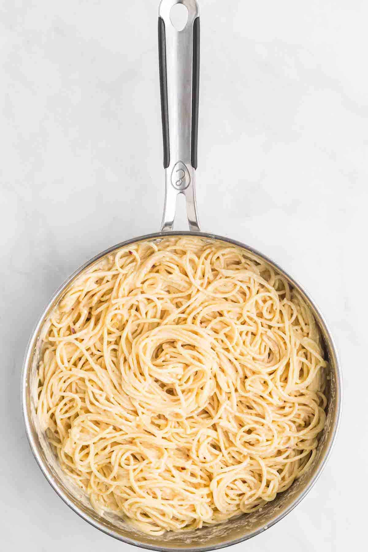 large skillet with the spaghetti noodles on top of the cream sauce.