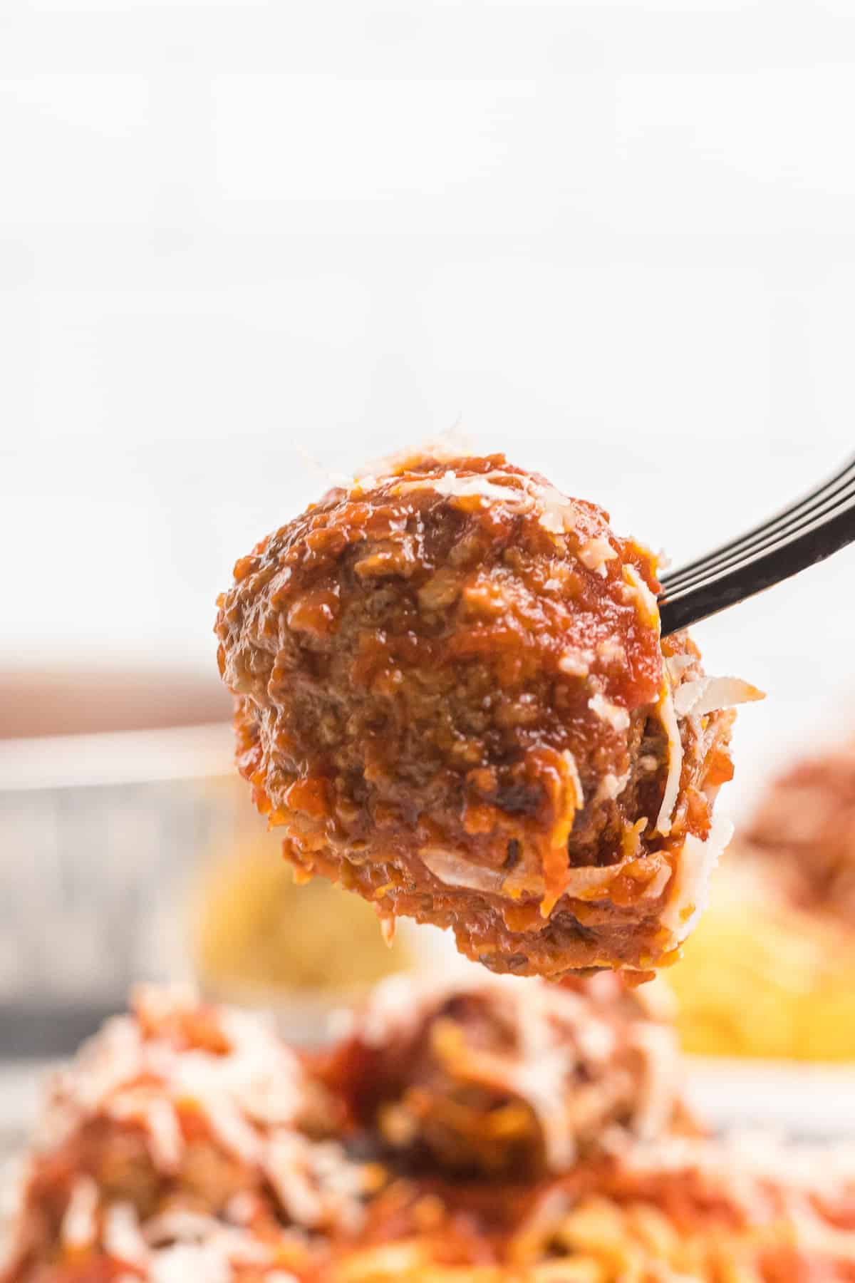 meatball on a fork over plate full of meatballs and pasta.