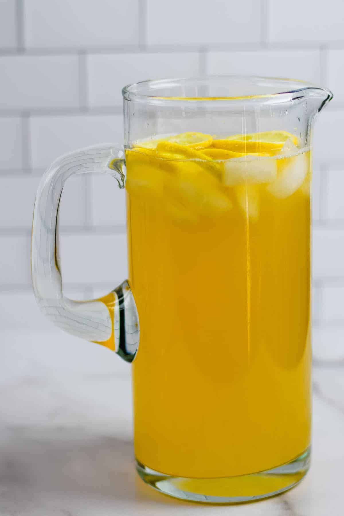 glass pitcher with lemonade, ice cubes, and lemon slices.