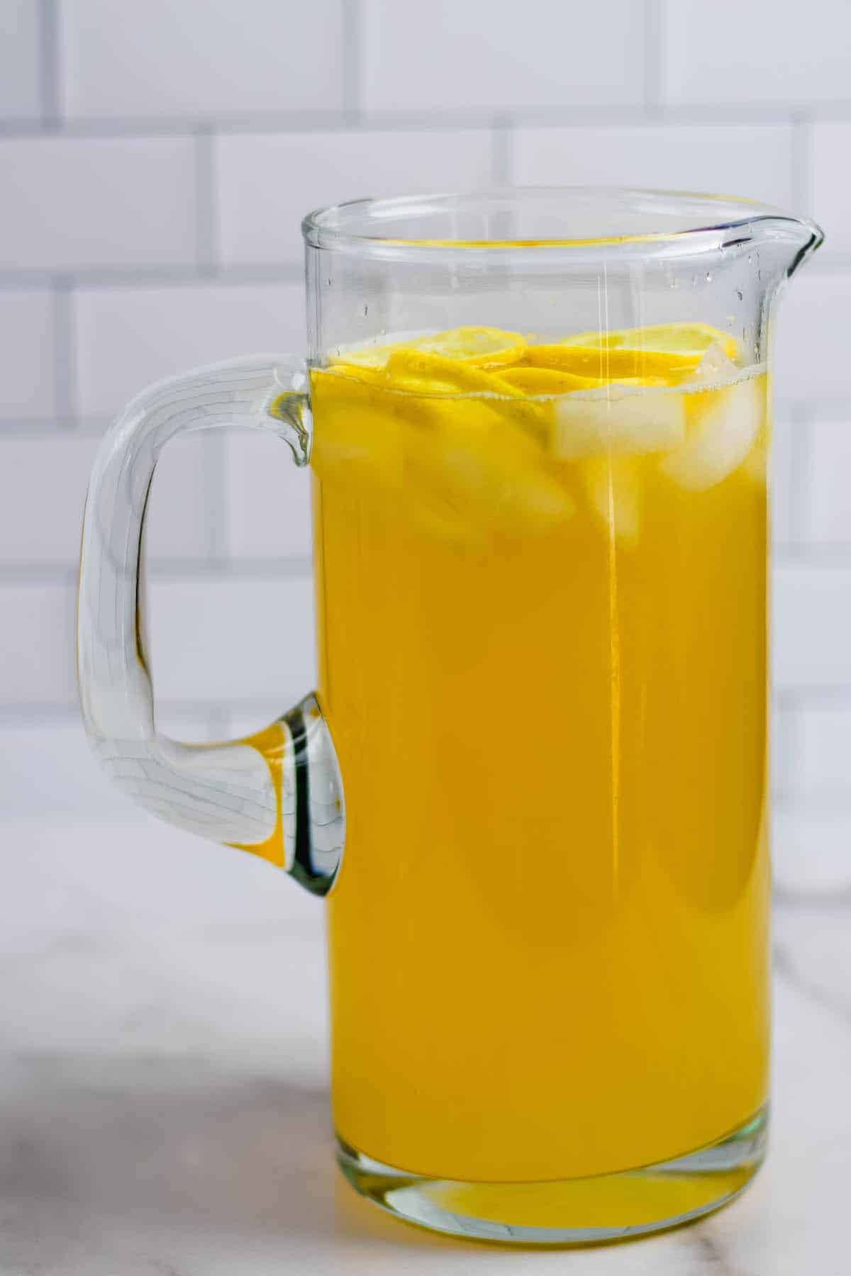 large glass pitcher of healthy lemonade with ice cubes and lemon slices.