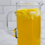 healthy lemonade in a glass pitcher with lemon slices and ice cubes inside.